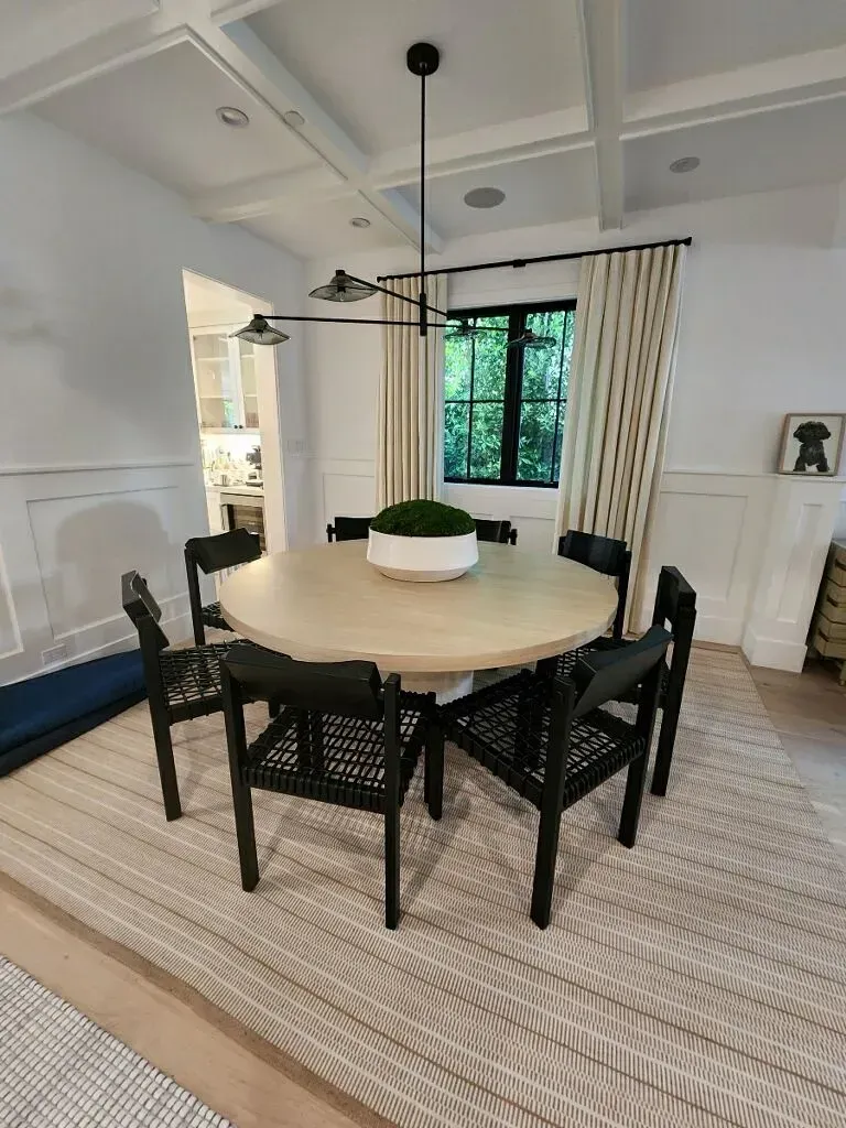 Modern dining room with round table, black chairs, striped curtains, and large window overlooking greenery