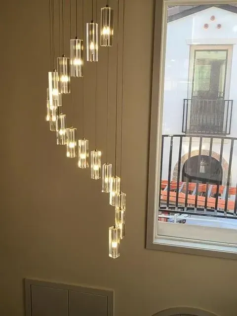 Modern pendant light with cascading clear glass tubes beside a window and balcony view