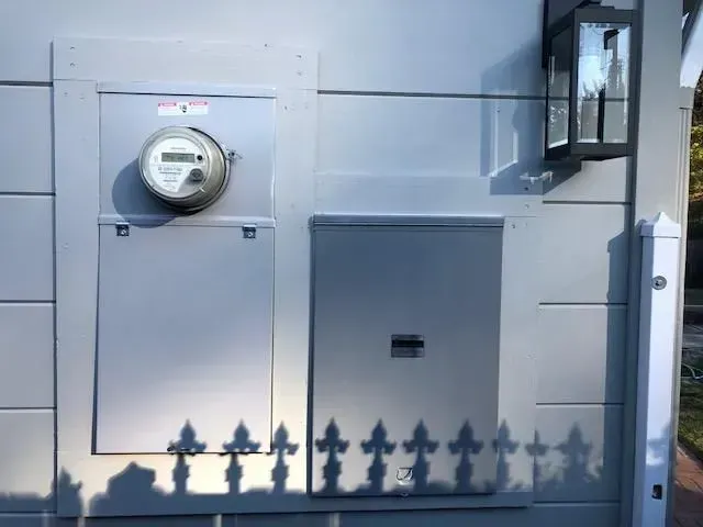 Gray utility panels and electric meters on a building wall, with a small lantern mounted on the right.