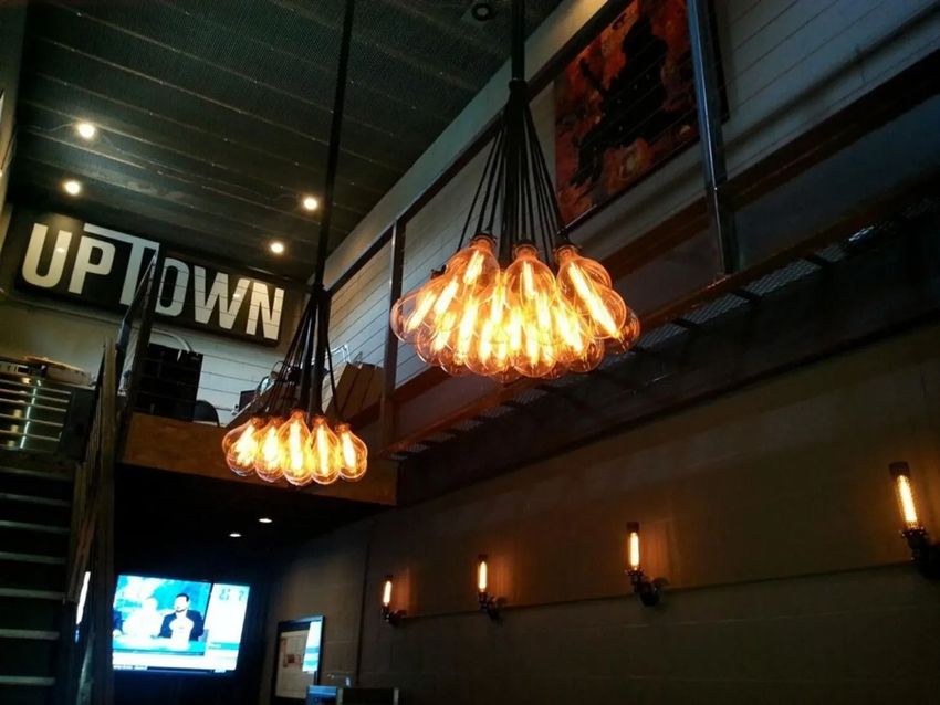 Dim restaurant interior with glowing pendant lights and an “UPTOWN” sign above a TV.