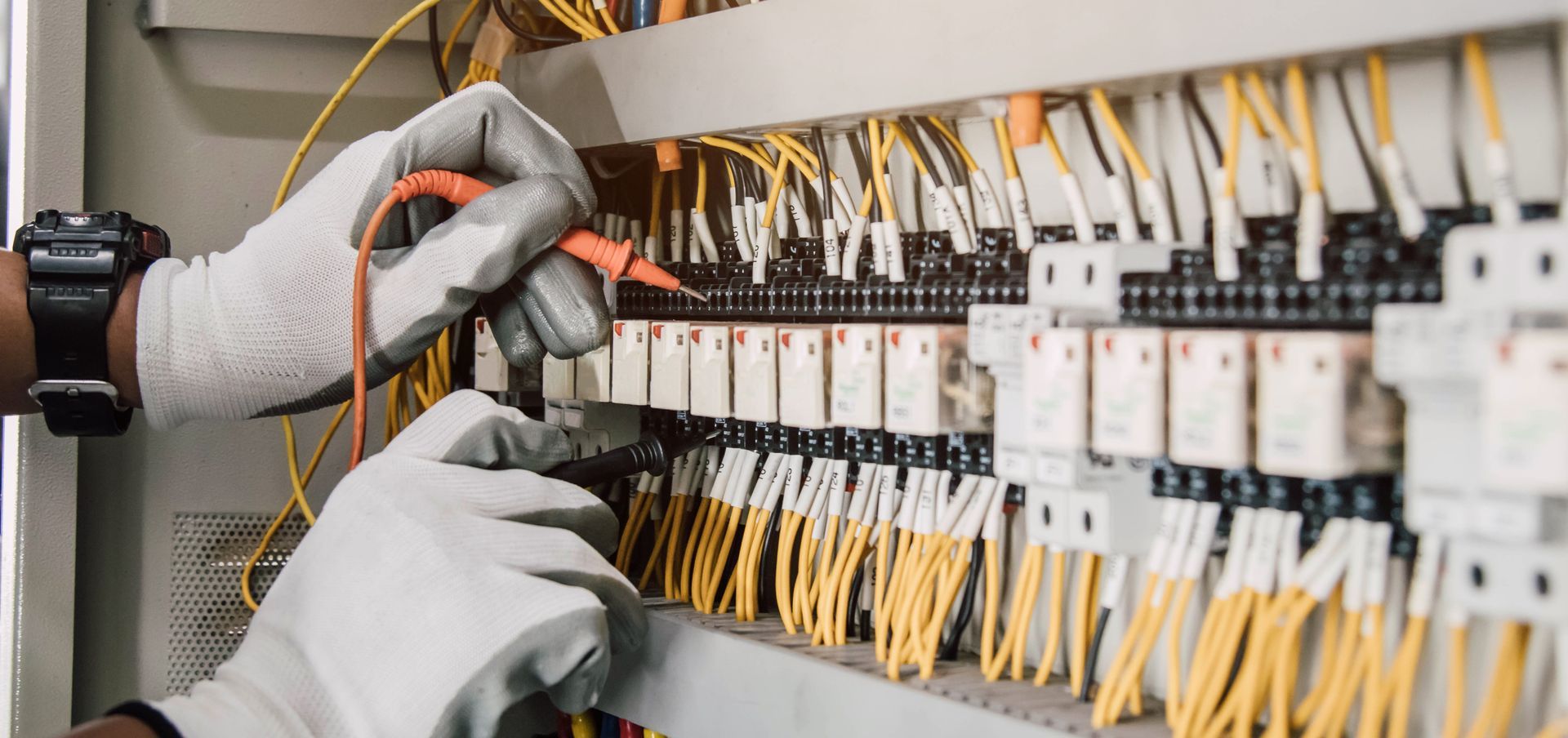 Gloved hands wiring an electrical control panel with rows of switches and cables