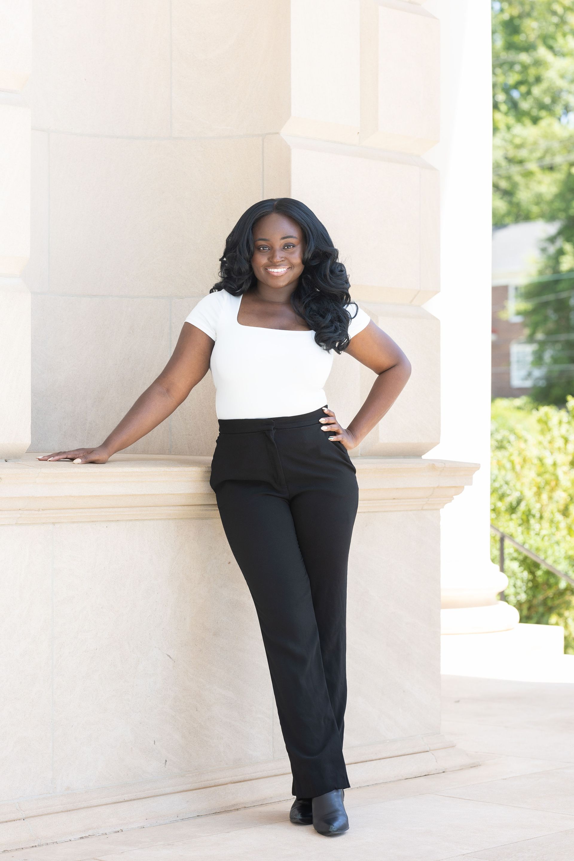 Dr. Elaine Johnson in white top and black pants poses by a stone column, smiling outdoors.