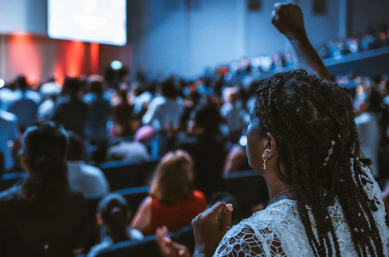 Woman with raised fist in a crowded auditorium, lit with red and blue.
