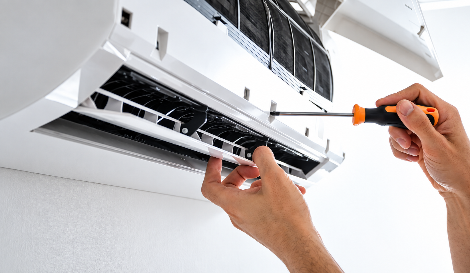 Manos reparando un aire acondicionado blanco de pared con un destornillador