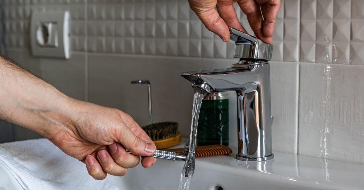 Unas manos giran un grifo cromado sobre un lavabo blanco, mientras corre el agua.