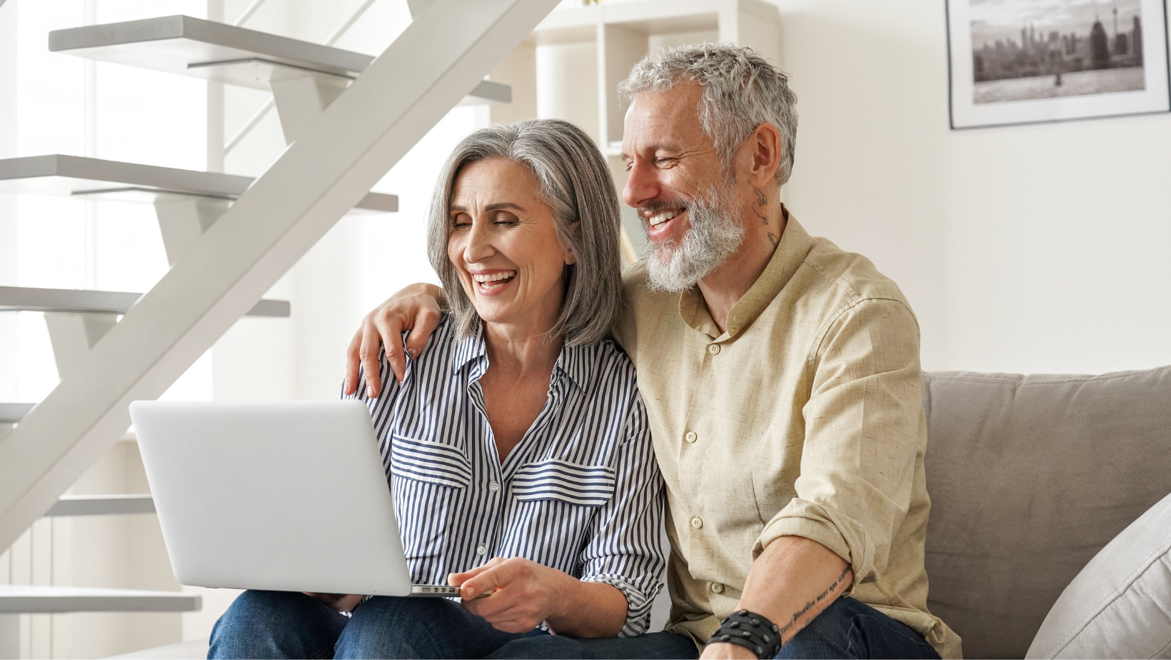 Smiling couple sitting on a couch with a laptop in a bright living room