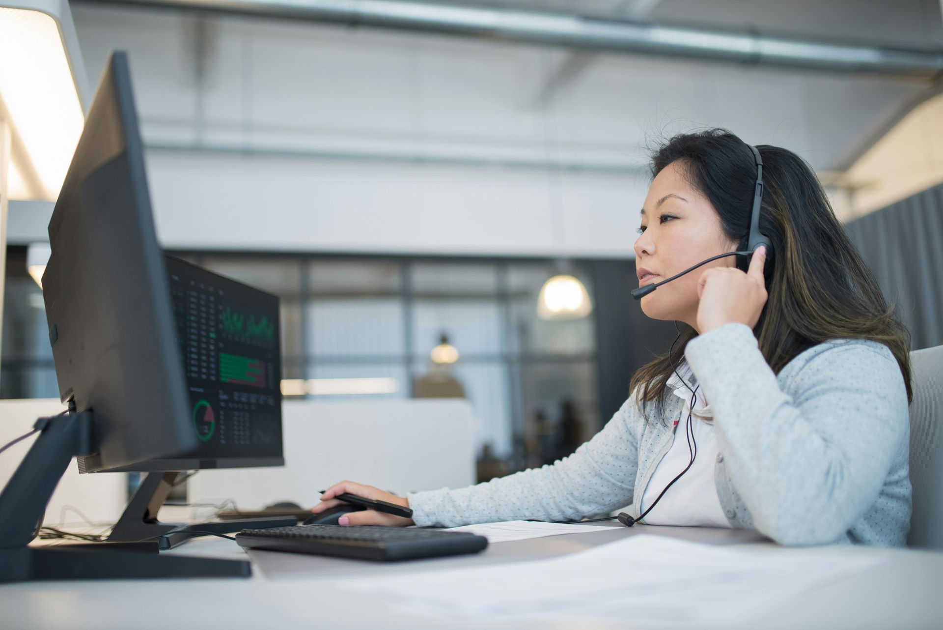 Mulher usando fones de ouvido, trabalhando em um computador e olhando para o monitor em um ambiente de escritório.