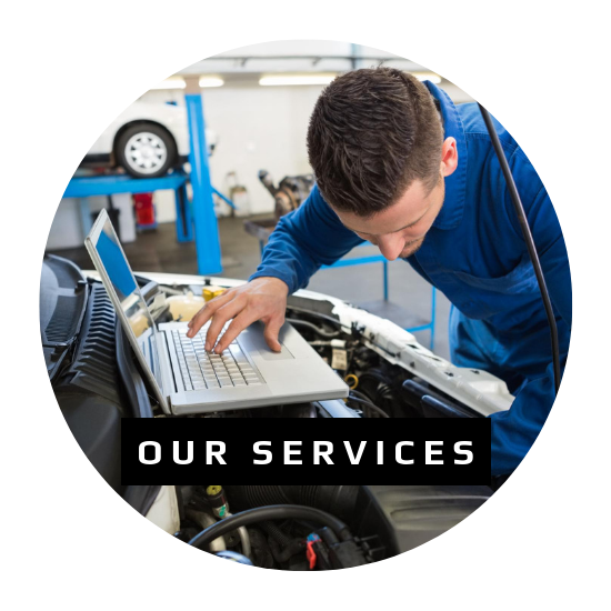 A technician in blue coveralls uses a laptop to diagnose a vehicle in a repair shop.