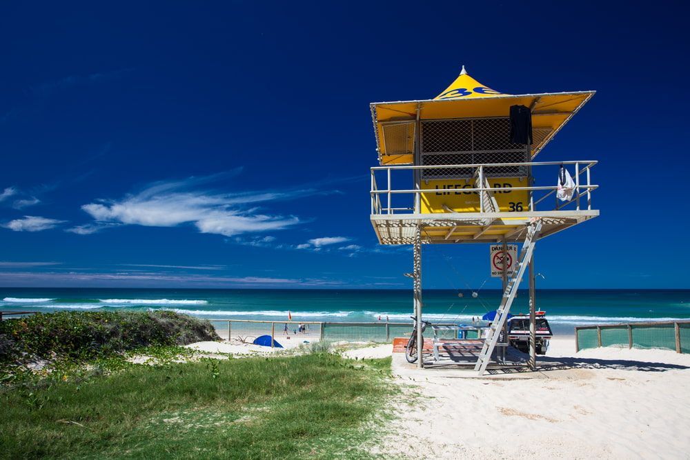 A Yellow Lifeguard Tower On A Beach Near The Ocean — Remedy Mobile Car Detailing in Broadbeach, QLD