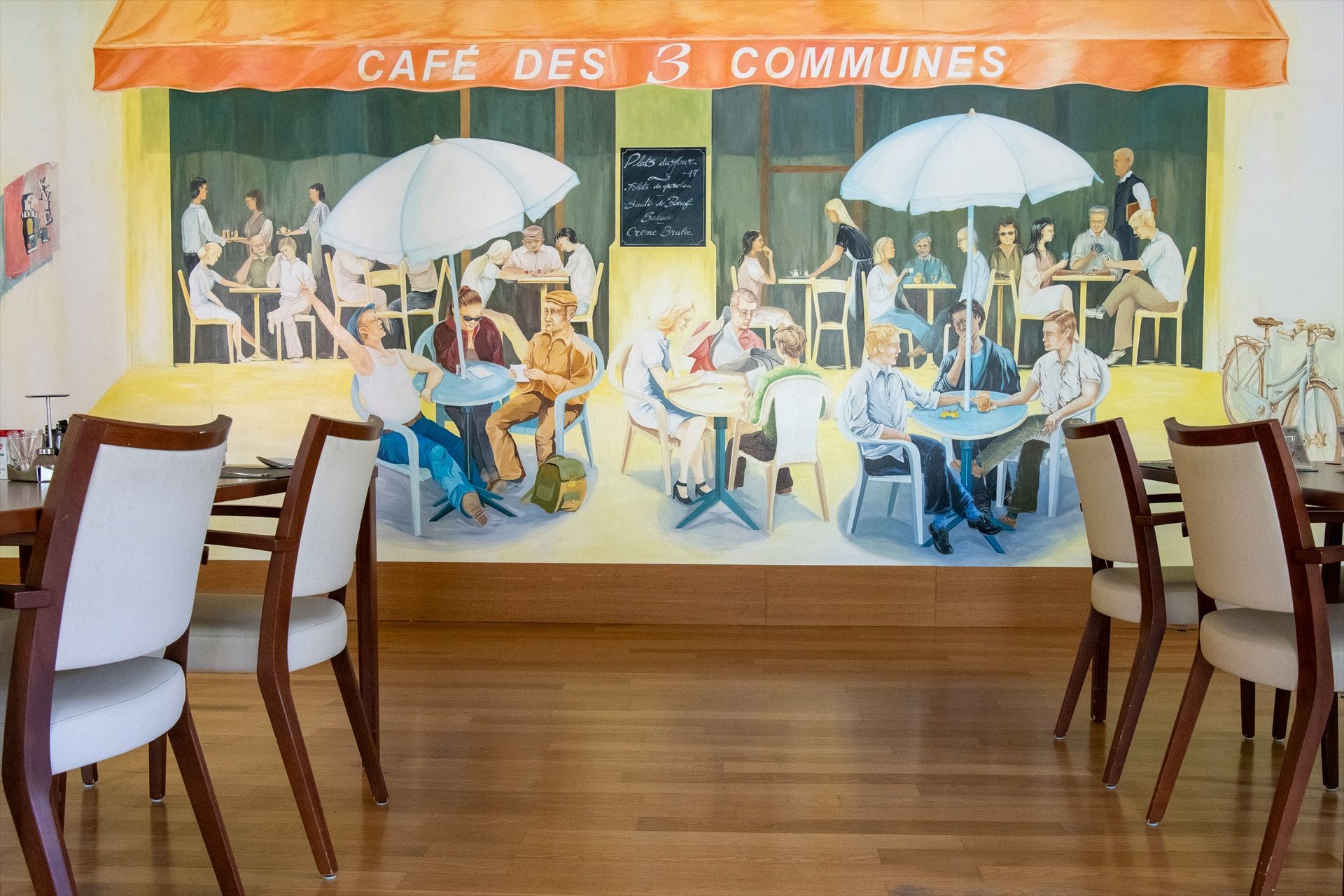 Une salle à manger avec des tables et des chaises et une grande fresque murale sur le mur qui dit café des 3 communes