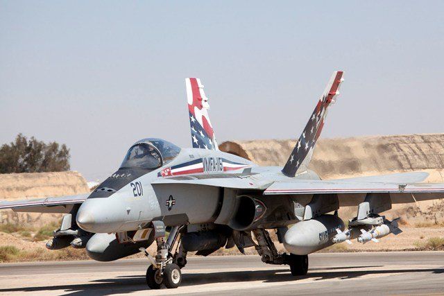 F/A-18F Super Hornet fighter jet on tarmac with patriotic tail art, under a sunny sky.