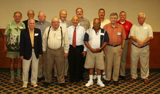 Group of men posing indoors. Most are wearing business casual attire, smiling.