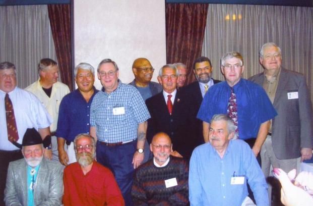 Group of men posing for a photo indoors, some wearing name tags.