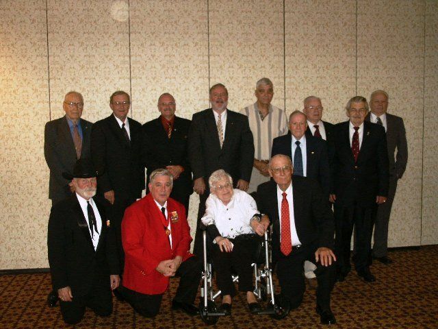 Group of men in suits posing for a photo, one in a wheelchair, indoors.