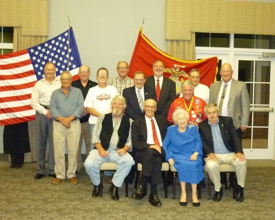 Group of people, mostly older men, pose for photo in a room with flags.
