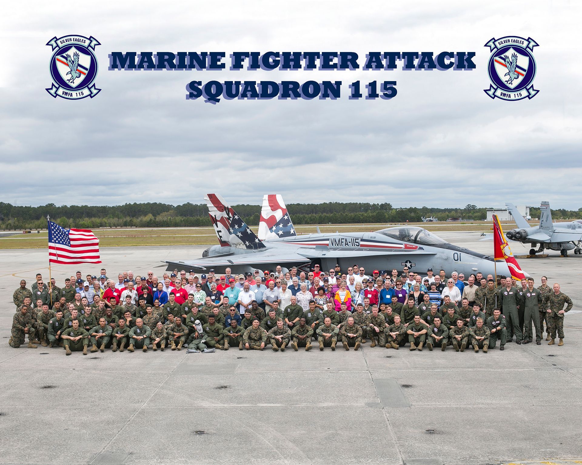 Marine Fighter Attack Squadron 115 stands in front of fighter jets on a tarmac with an American flag.