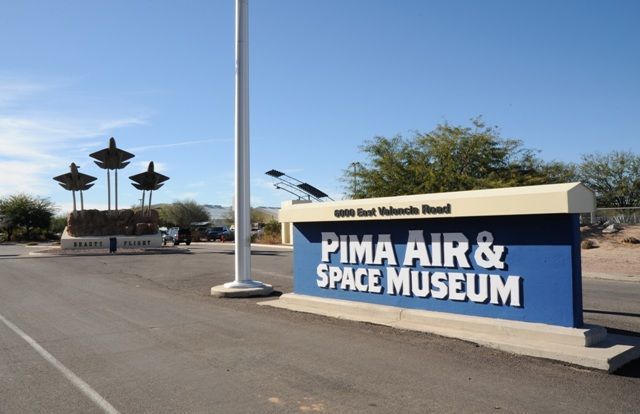 Sign for Pima Air & Space Museum on East Valencia Road, with blue text, three abstract sculptures, and clear sky.