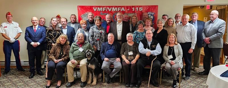 Group of people posing for a photo in a room with a banner that says
