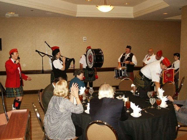 Scottish bagpipe band performs at a formal dinner, people seated at tables, one person singing.