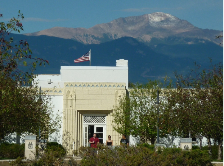 White building with American flag; mountains in background. People stand near doorway.