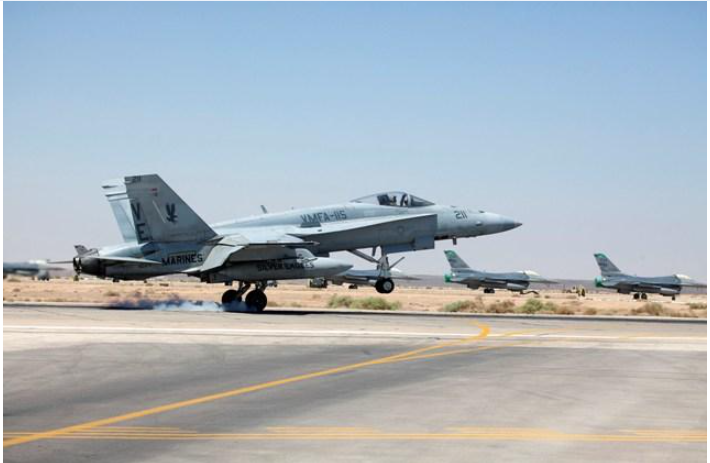 Fighter jet landing on runway, other jets in background, sunny day.