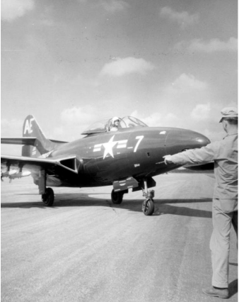 Navy fighter jet on a runway, being directed by a person in uniform.