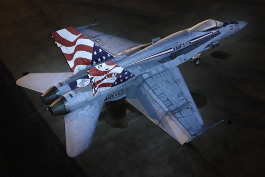 Top-down view of a US Navy F/A-18F Super Hornet jet with an American flag paint scheme on its tail.