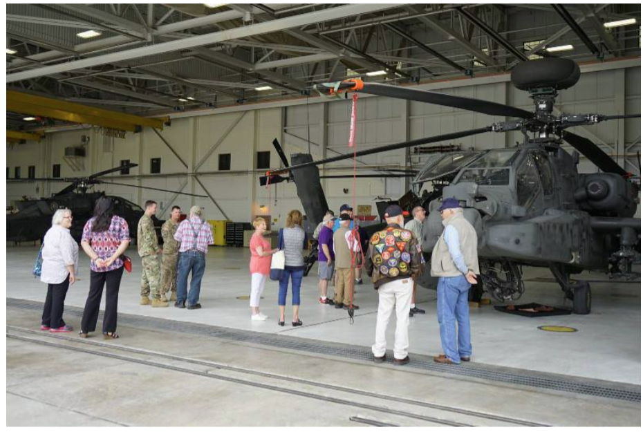 People observing military helicopters inside a hangar.