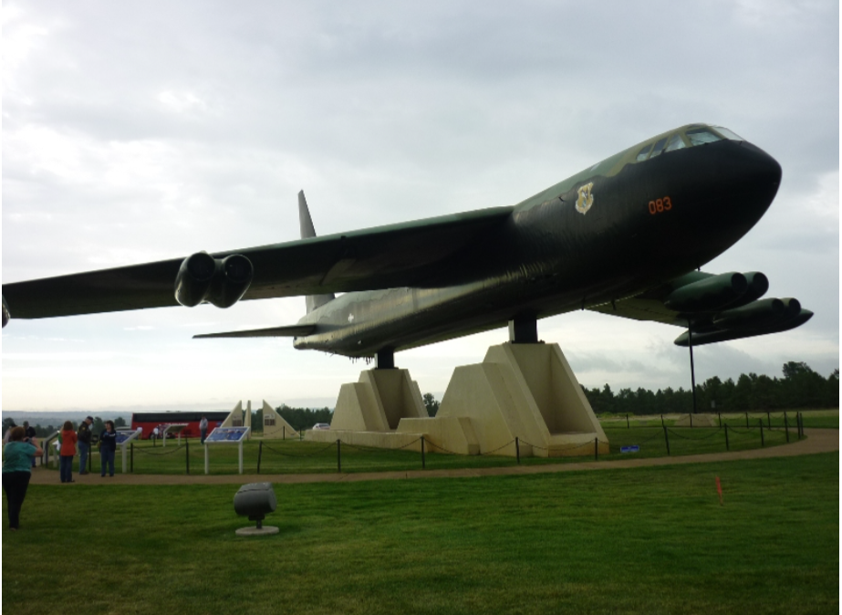 Black B-52 bomber on display, mounted on concrete supports in a grassy area with some visitors.