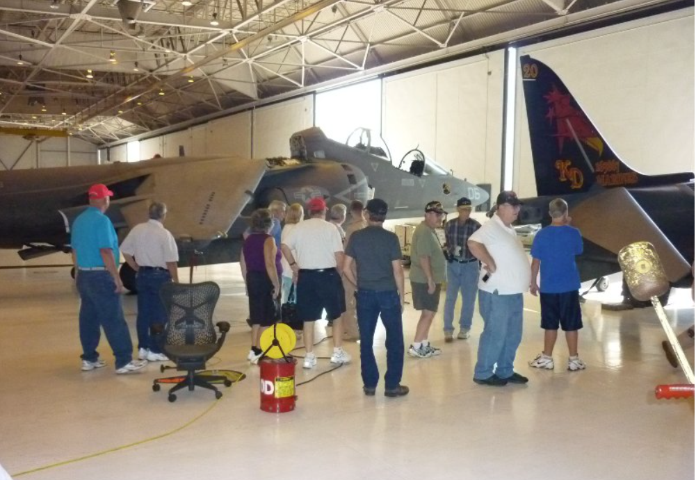 Group of people touring a large airplane inside a hangar; red, black, and tan colors.