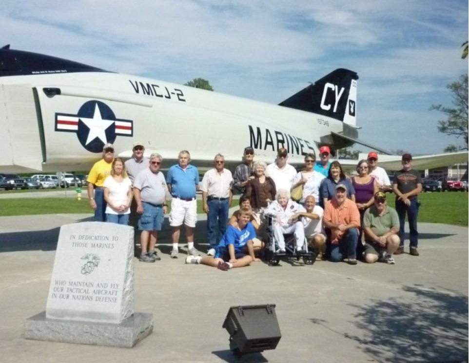 Group of people posing by a Marine Corps F-4 Phantom II jet at a memorial.