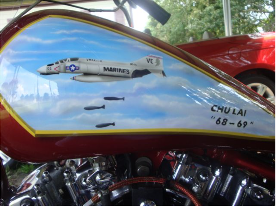 Motorcycle gas tank with a painted fighter jet in a blue sky;