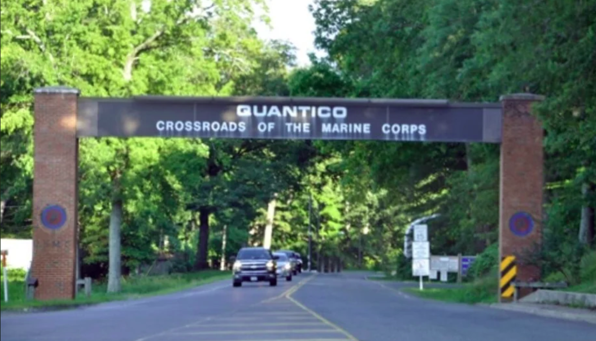 Entrance to Marine Corps Base Quantico, Virginia, with archway sign and passing vehicles.