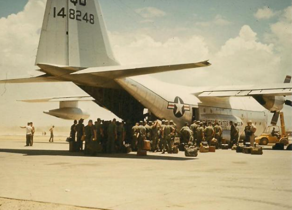 Soldiers boarding a C-130 transport plane on an airfield. The plane is white with US markings.