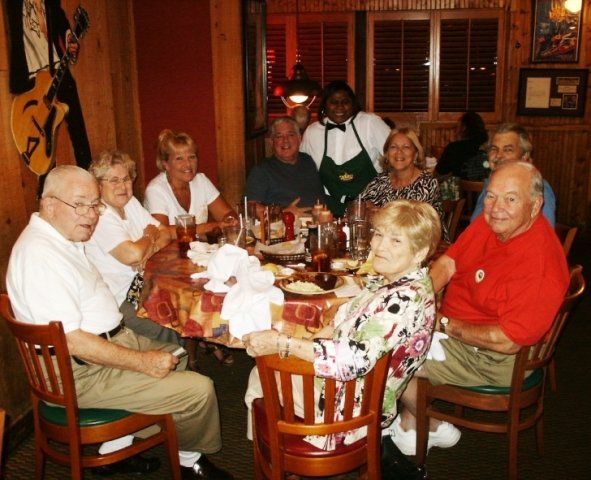Group of people dining at a restaurant, seated around a table. A waitress smiles in the background.