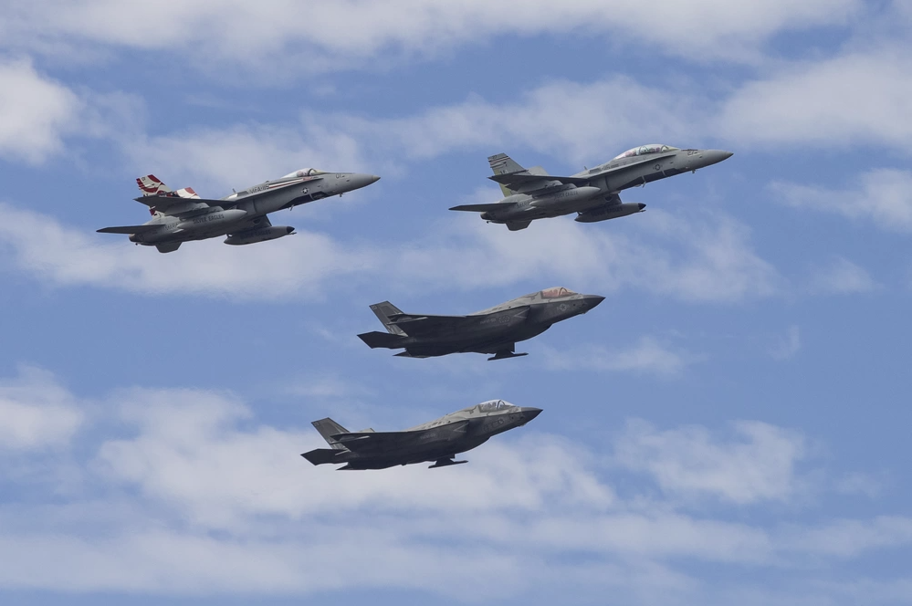 Four military jets flying in formation against a blue sky, including F-35s.