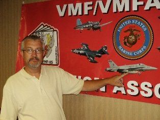 Man pointing at airplane graphic on a red Marine Corps banner.