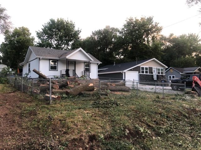 Homes after tree removal; logs in the yard, fence, and a small excavator.