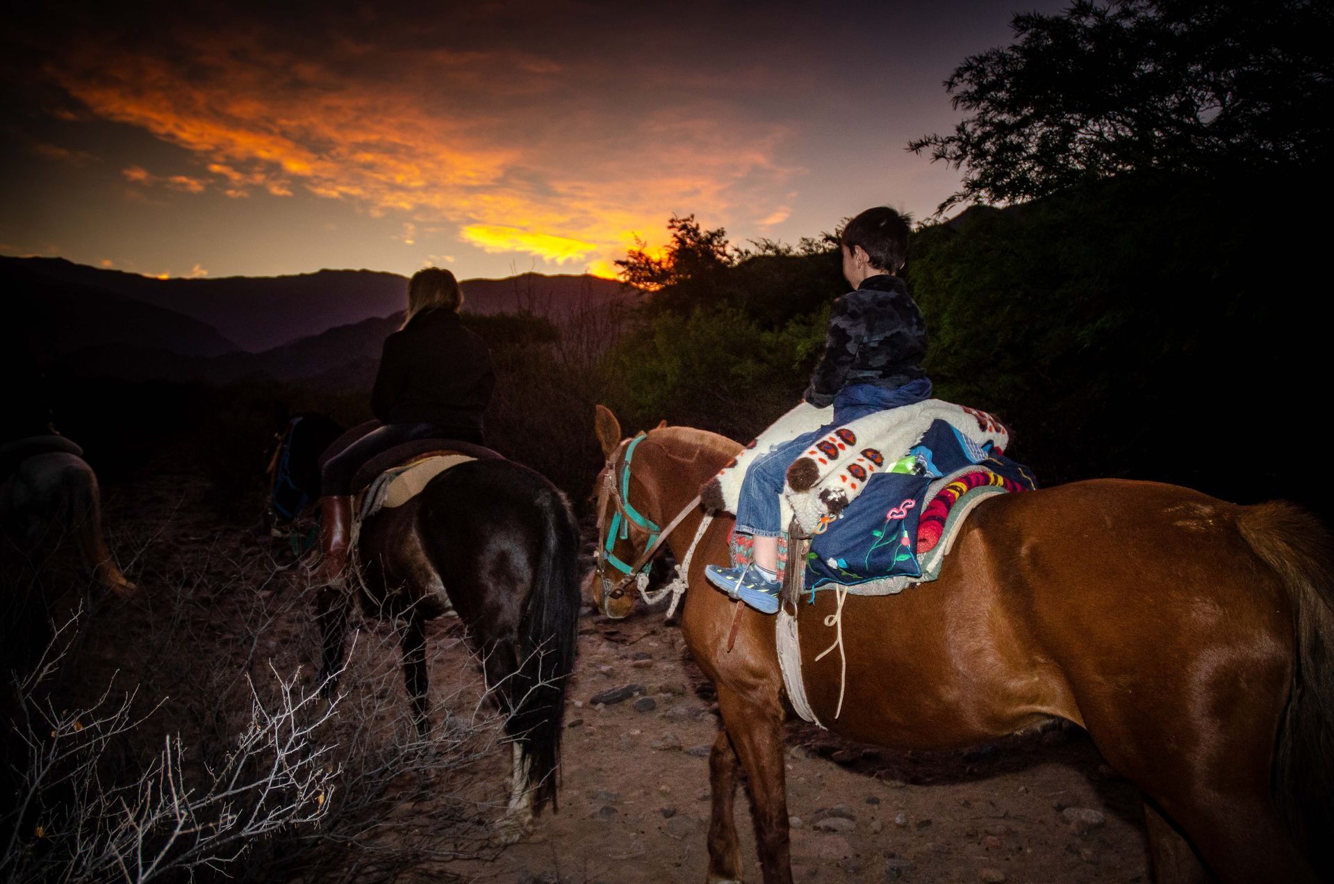 Dos personas montan a caballo en las montañas al atardecer.