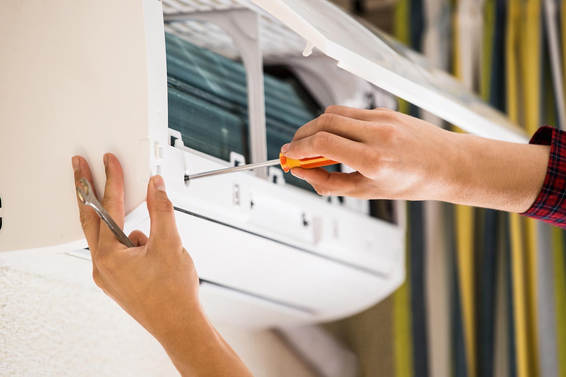 Hands installing or repairing a wall-mounted air conditioner with a screwdriver
