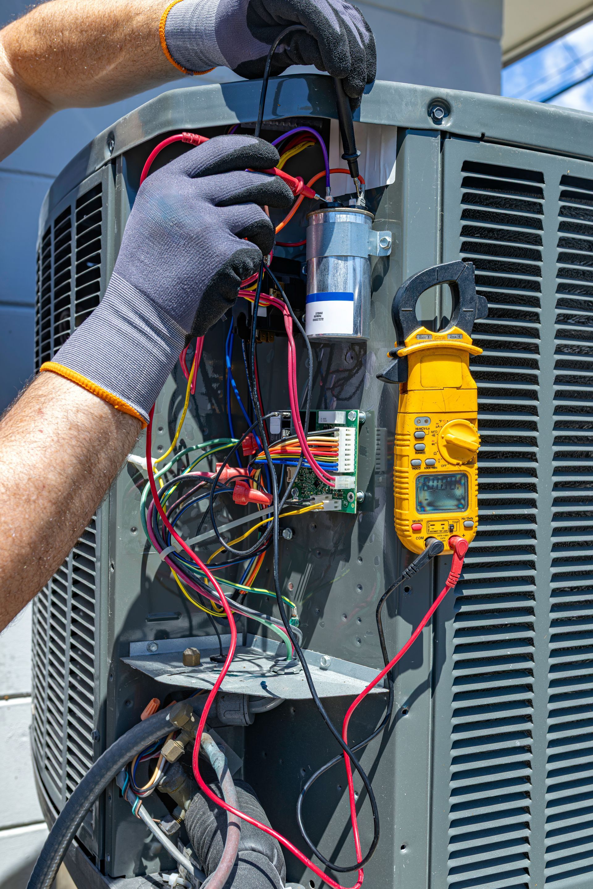 Technician testing condenser wiring with a multimeter during an emergency AC repair.