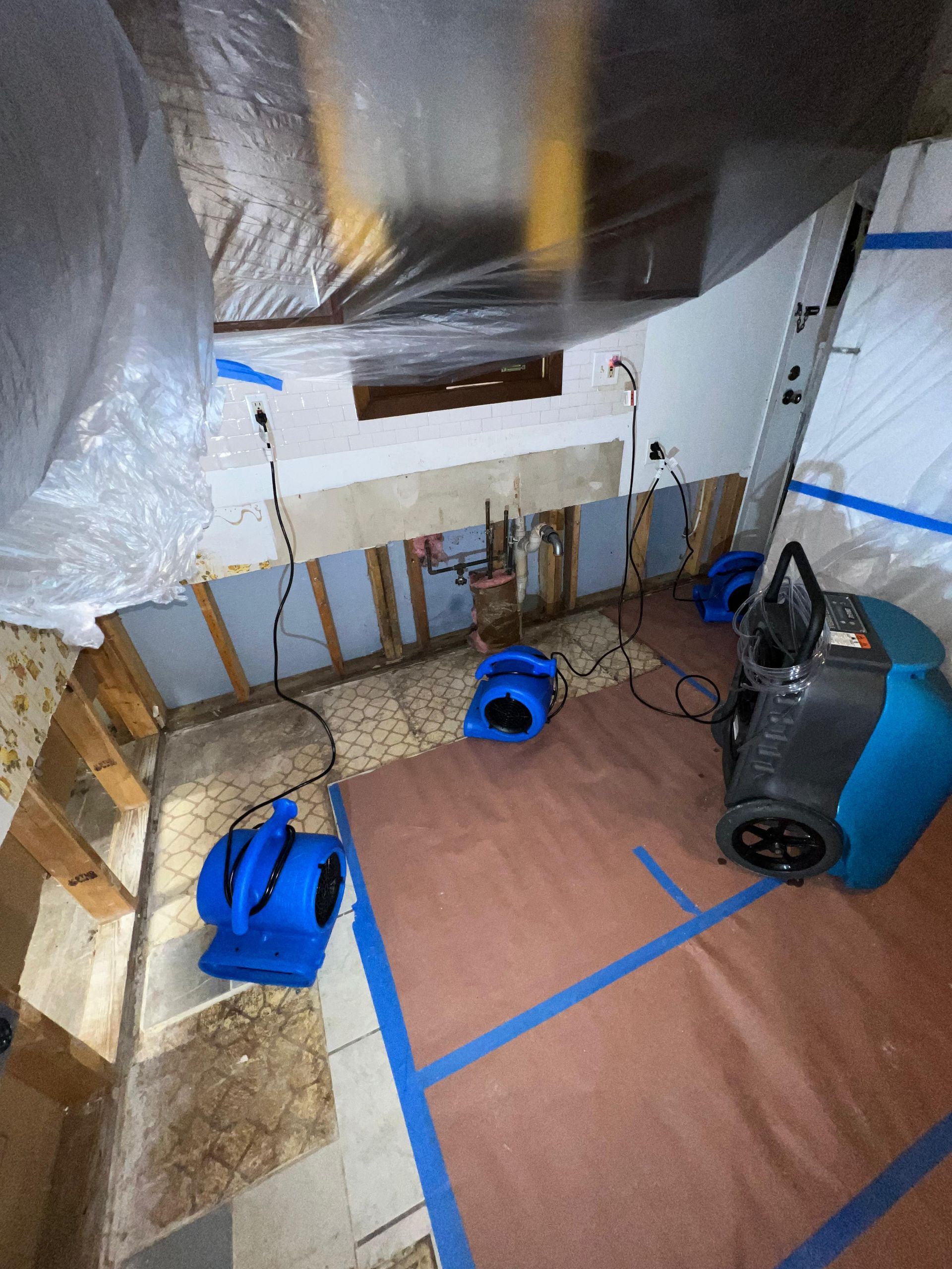 Small unfinished basement with exposed walls, taped floor area, blue tools, and a wet-dry vacuum.