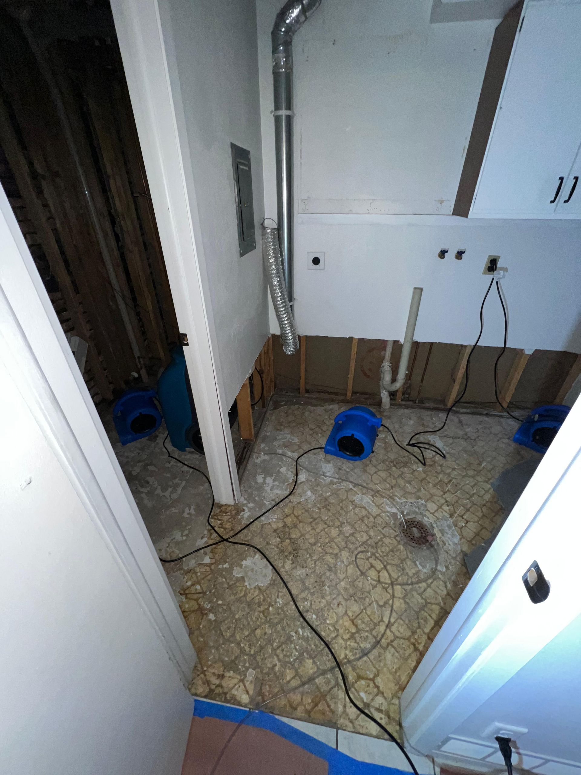 Messy room with wires, tools, and debris on a tiled floor near cabinets and a doorway.