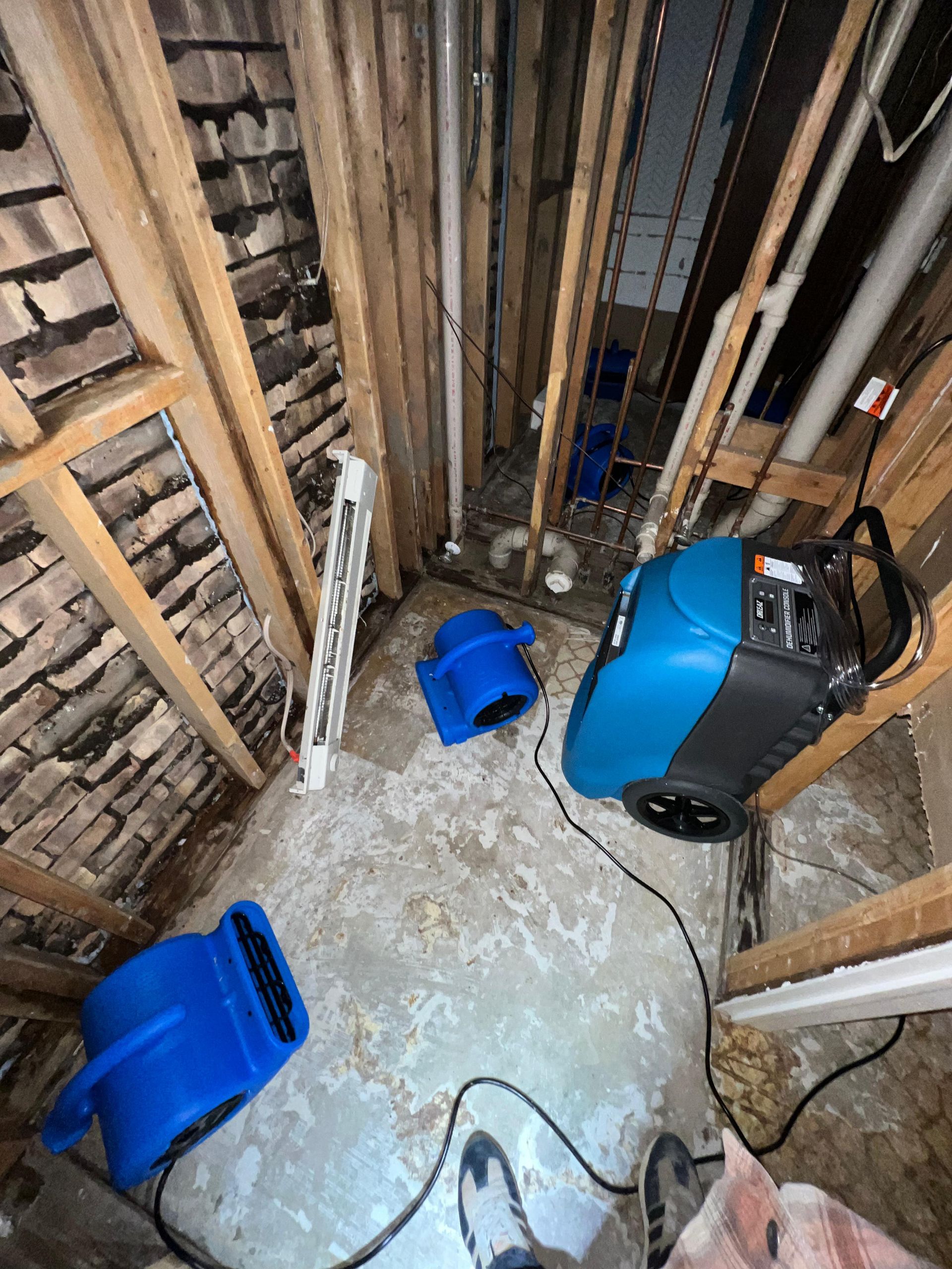 Basement or crawlspace with exposed studs, debris, blue buckets, and a blue portable machine on the floor