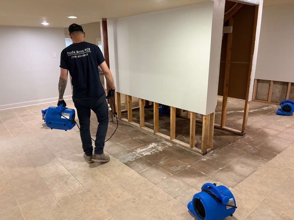 Worker carrying a blue blower in a partially gutted room with exposed wall studs