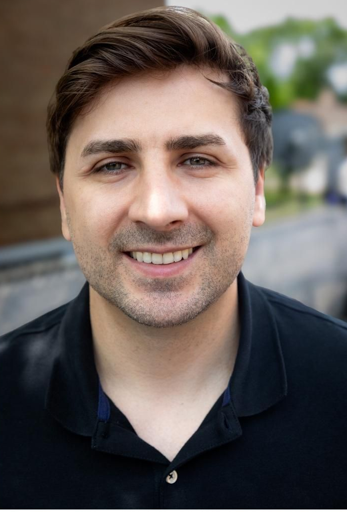 Smiling man in a dark shirt outdoors with a blurred background