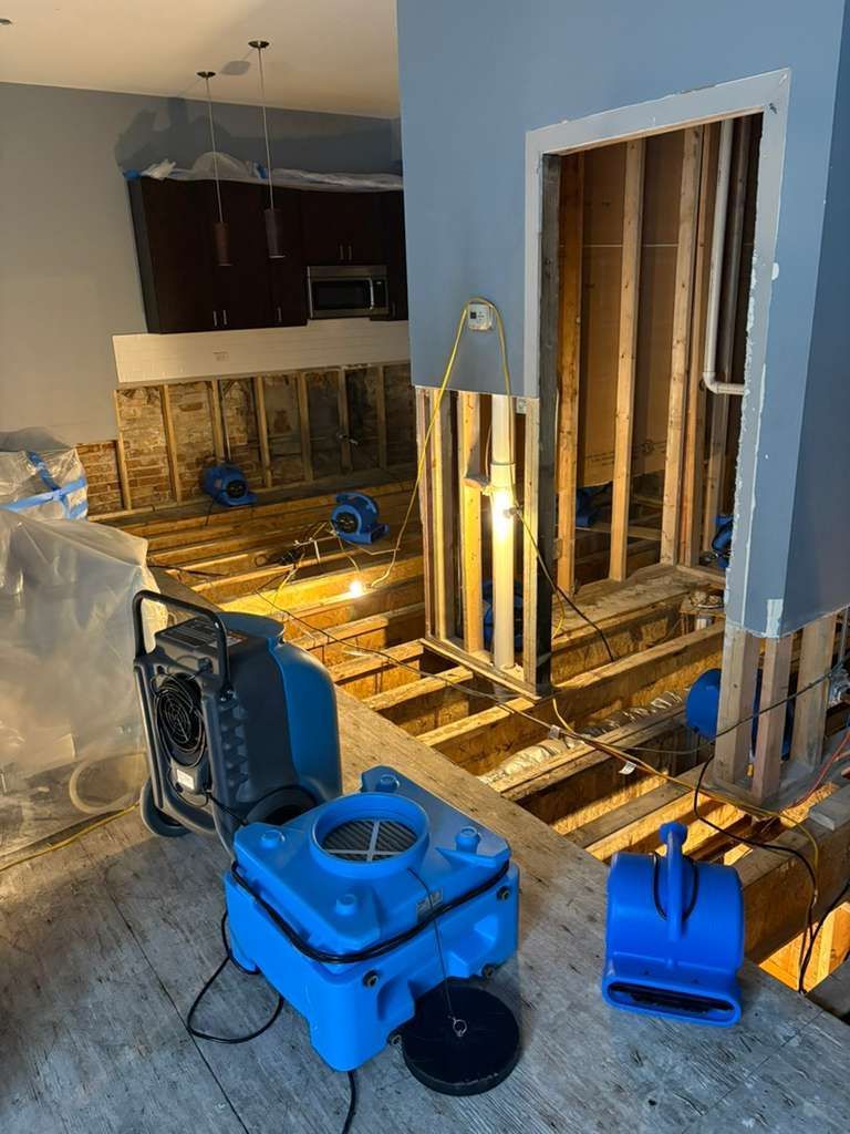 House interior under renovation with exposed floor joists, tools, and blue cleaning equipment.