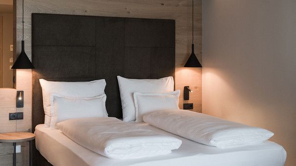 In einem Hotelzimmer steht ein Bett mit weißen Laken und Kissen.