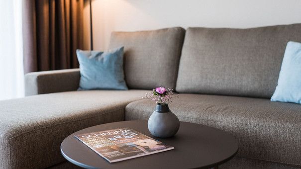 Ein Wohnzimmer mit einer Couch und einem Tisch mit einer Vase mit Blumen darauf.