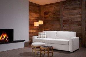 ein weißes Schlafsofa steht auf einem Holzboden vor einer Holzwand bei einem Kaminfeuer. 